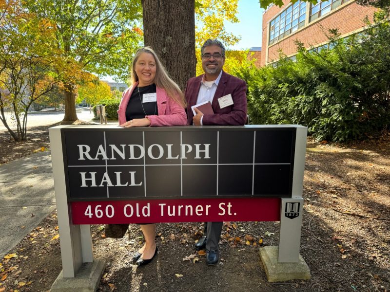 (From left to right) Kimberly ‘00 and Amit Puri ‘99 stand behind the Randolph Hall sign, commemorating where the couple met.