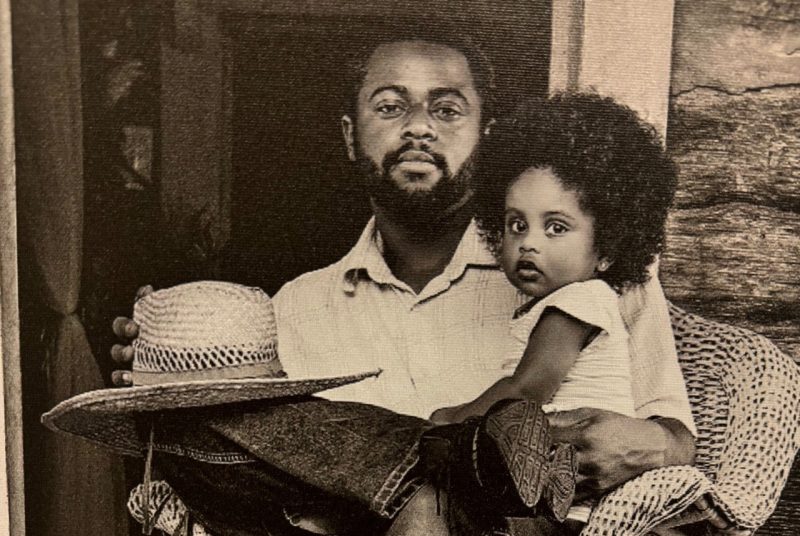 Black man sitting on porch with black child in his lap.