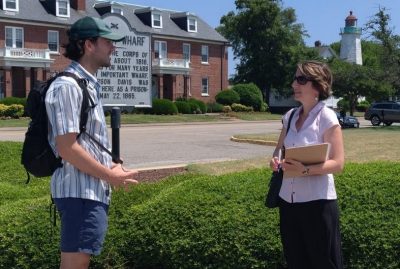 Two people stand facing one another in front of a brick building.