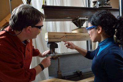 Two people examine a piece of wood set on a machine. 