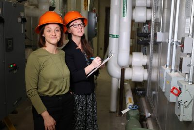 Two people wearing hardhats stand next to a large machine.