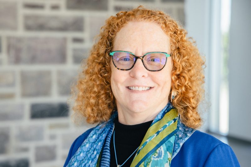 A portrait of a woman with red, curly hair and glasses