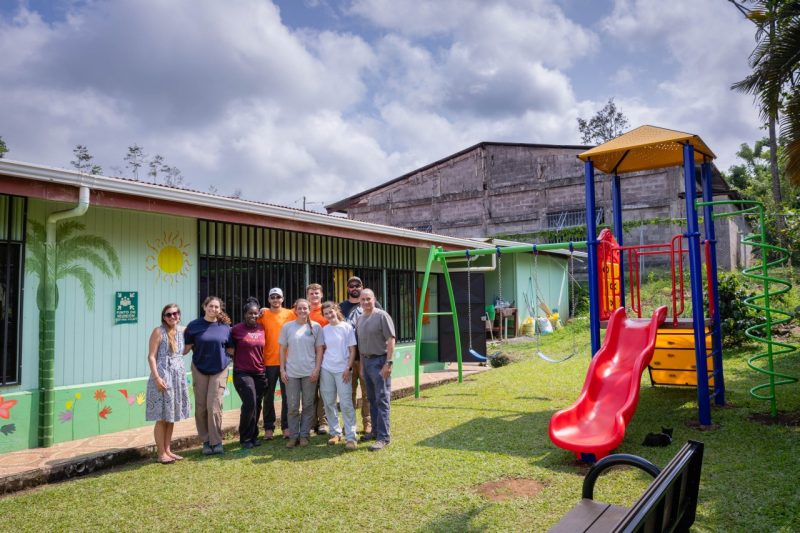 A group of students smile next to a Costa Rican playground that they built.