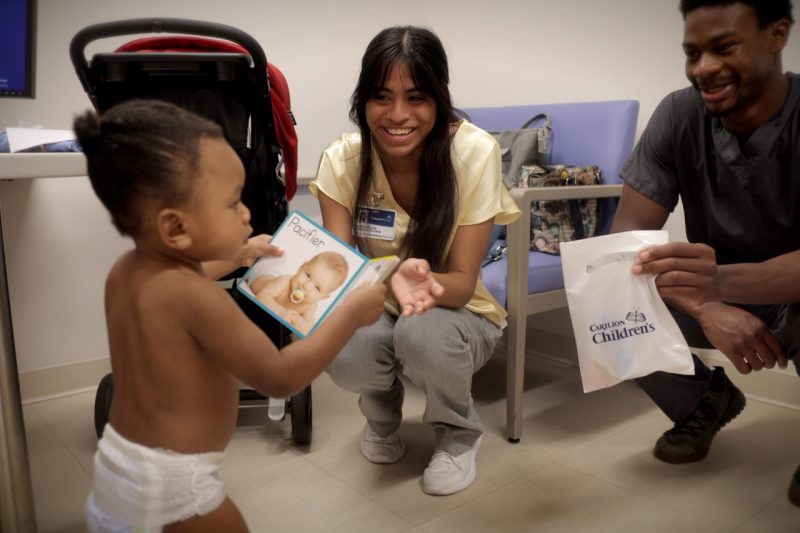 A pediatric patient looks at a book in an exam room with a young woman and man smiling on.