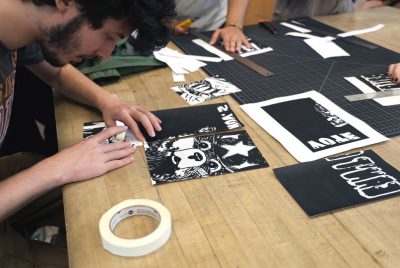 A student sits at a wooden table putting together sections of paper that form a drawn image of Smokey the bear when assembled.