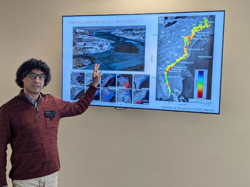 Manoochehr Shirzaei gestures at a screen with the a graphic and the title: "Sinking land on the U.S. East Coast."