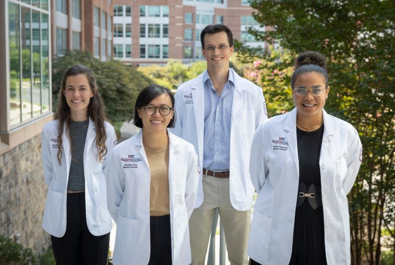 Four medical students wearning their white coats standing side-by-side outdoors.