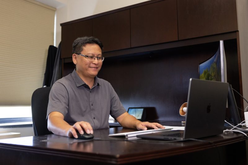 Yinlin Chen sits at his desk and is smiling at his computer screen.