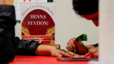 A sign reads "henna station" a hand is seen getting henna applied to it