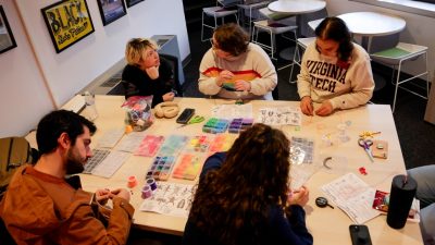 Five people sit around a table making a craft with beads