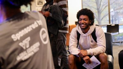 Black male students sitting and smiling. In the foreground the back of the Hokie Culture Crawl shirt can be seen