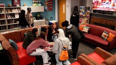 Six people gather around a small table. The table appears to hold food they're sharing.