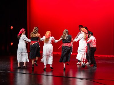 A group wearing bandanas and dance in a circle on stage