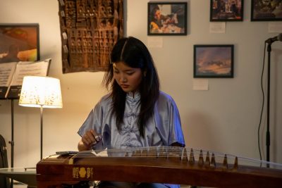 A woman wearing traditional silk outfit plucks the strings of traditional Asian wooden instrument