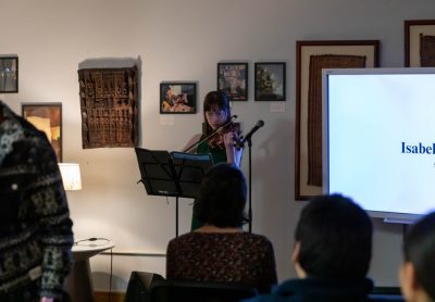 Woman plays a violin in front of a small seated crowd