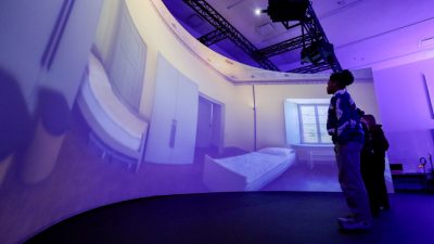 Silhouettes of people looking a room displayed on a large floor-to-ceiling screen