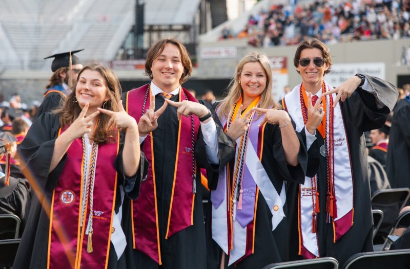 Four recent graduates pose for a photo in Lane Stadium