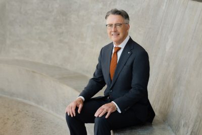 President Tim Sands sits wearing a dark suit and orange tie. 