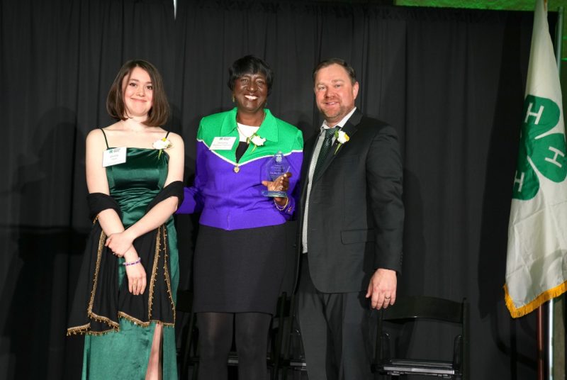 Three people stand together, displaying a glass award.