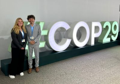 Woman and man in professional dress stand in front of large letters.