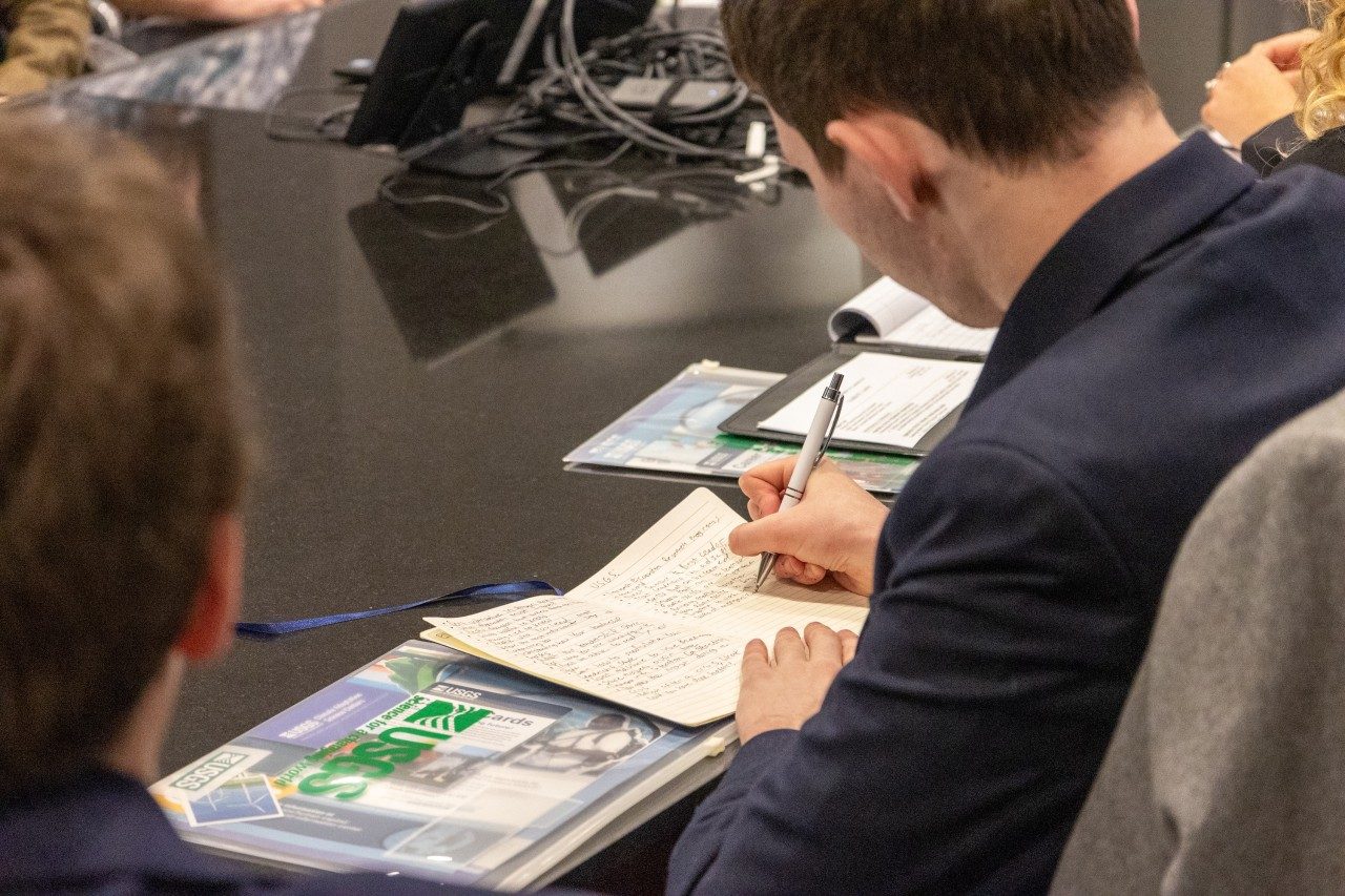 A student takes notes in a notebook at a table.