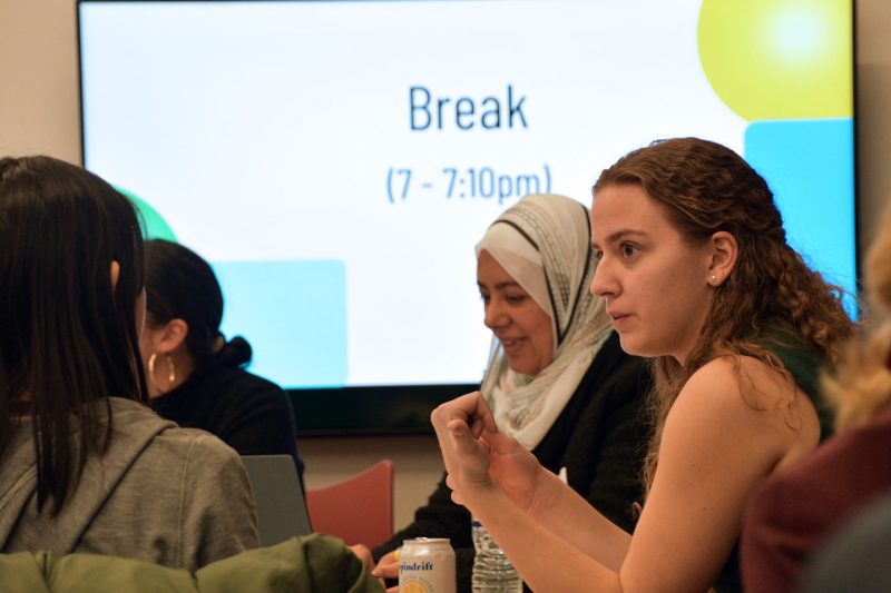 Several women have a discussion while sitting at a classroom table.