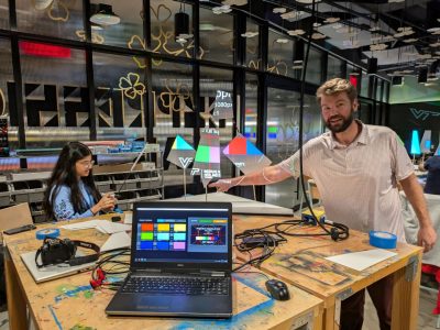 Alexander Rudd (at right) demonstrates projection mapping onto suspended geometric forms. A participant (at left) works on a projection. Photo by David Franusich for Virginia Tech.