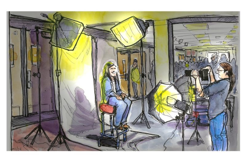 Ink and watercolor sketch of a student having a headshot made by a photographer during the Business Horizons Career Fair in Squires; the sketch has a lot of lights and a backdrop