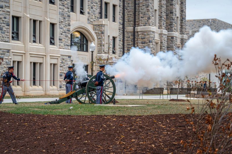 Skipper fires and smoke and flames shoot from the barrel. Cadets completing Caldwell March can be seen in the background.
