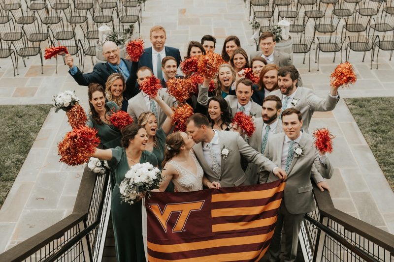 A group of people gathered around a couple celebrating their wedding, holding a hokie nation flag