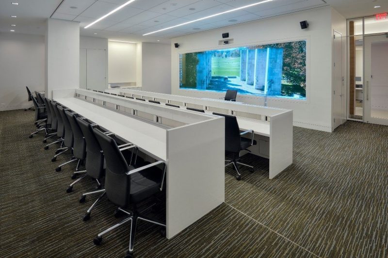 A meeting room with rows of white desks and black chairs and a large screen with a photo of the Virginia Tech Pylons on display.