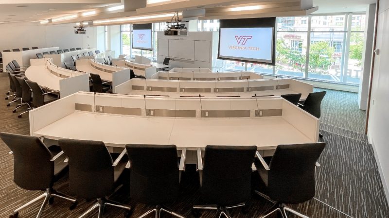 A large conference room with white desks, black chairs, and pull-down screens with the Virginia Tech logo.