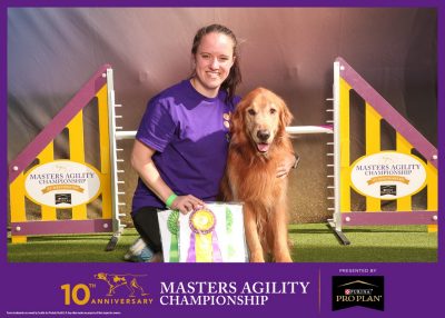 Person and dog pose in front of agility equipment.