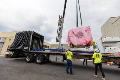 A crane unloads part of a MRI machine from the back of a flatbed truck.