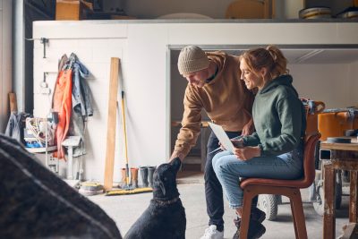 A man and woman (at right) petting a black lab (at left) in a wood working shop