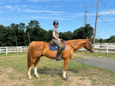 Esther Vergel sitting on a horse outside in a fenced in grassy area