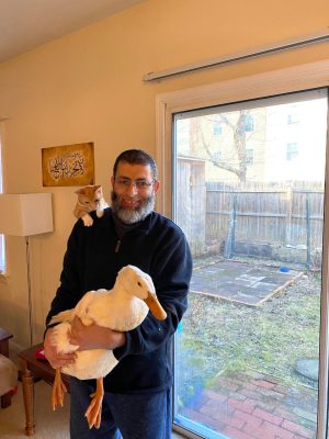 Fawzy Elnady holding a white duck with his cat on his shoulder 