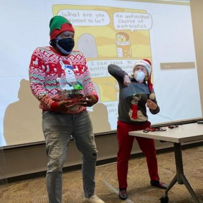 Two people in holiday sweaters in front of a projector.