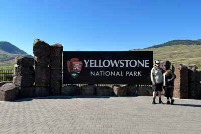 Karson Sluss standing in front of the Yellowstone National Park sign with another person.