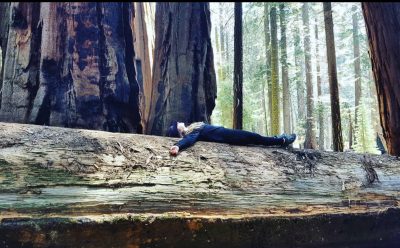 Skylar Moiseeva laying on top of a large fallen tree.