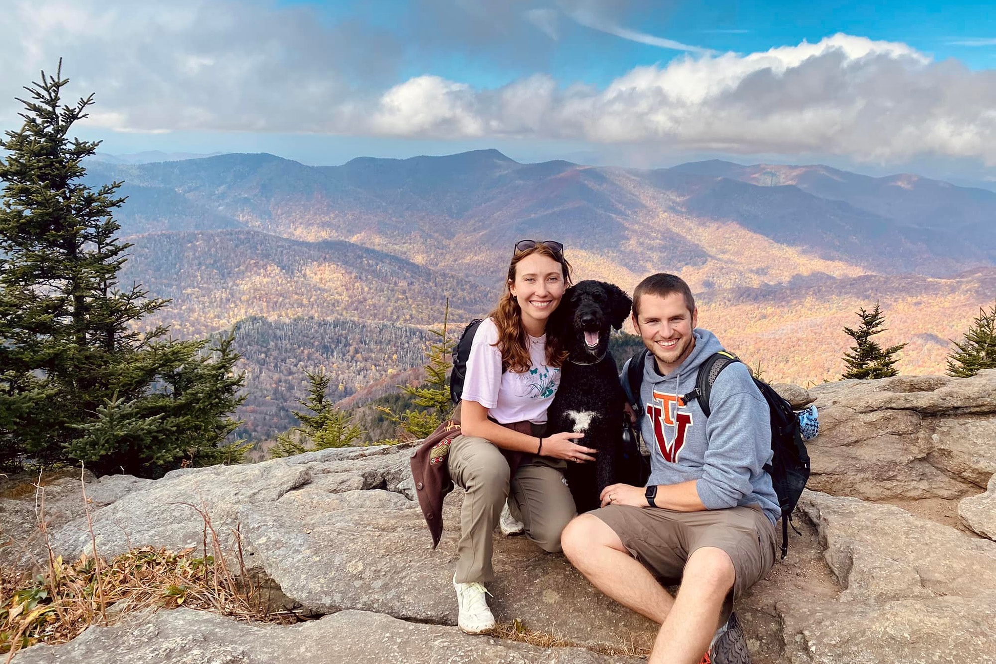 Alexandra Fox (at left) posing on a rock with a black poodle (at center) and a person (at right)