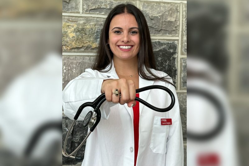 Lauren Maghak wearing a white coat holding her stethoscope