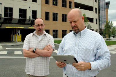 Two men stand outside looking at an iPad.