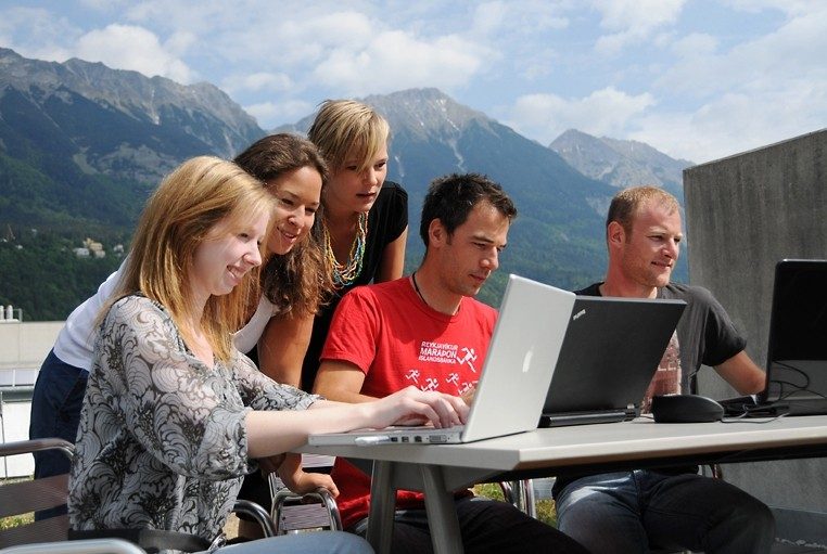 Five students sit on a rooftop patio with their laptops overlooking the alps in Innsbruck, Austria.