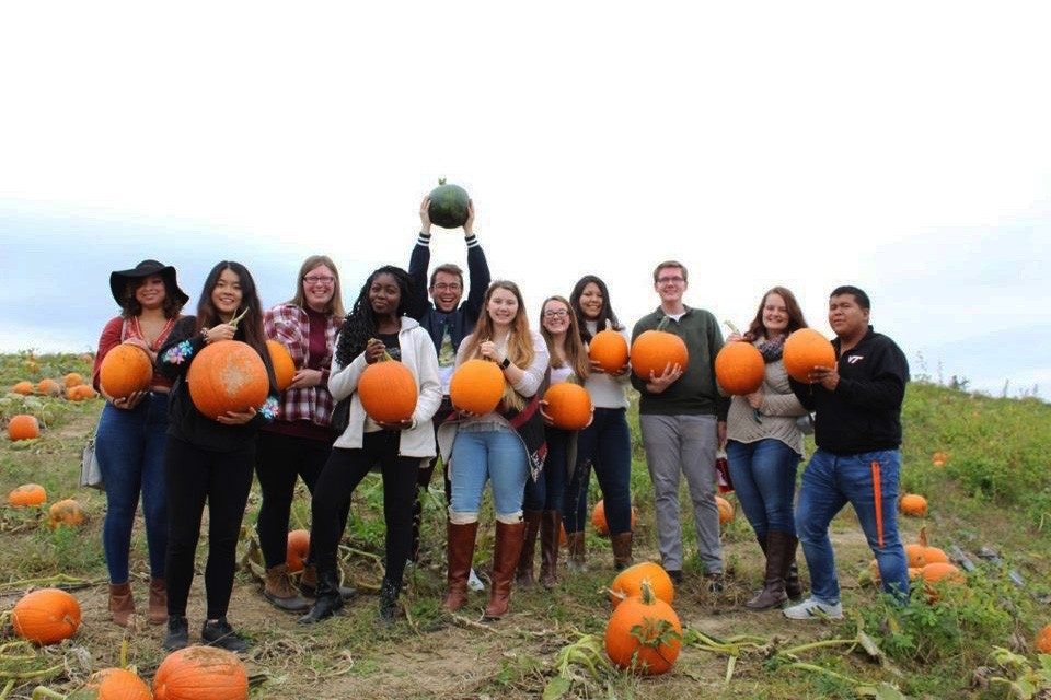 Mason Stoecker (center, holding up green pumpkin) poses with transfer students in a pumpkin patch.