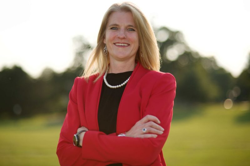 Robin Queen, professor of biomedical engineering and mechanics, stands outside in front of blurry trees, wearing a red suit jacket over a black shirt.