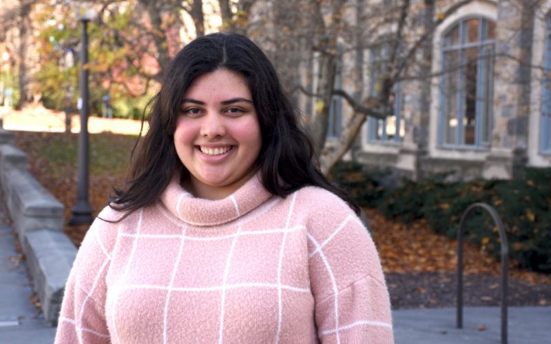 A young woman with jet black hair wears a pink checkered sweater.