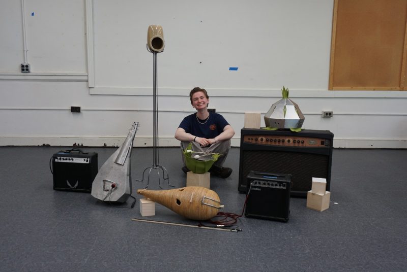 Claire Suess sits on the floor with legs crossed, among some of her original instruments, and electronic equipment