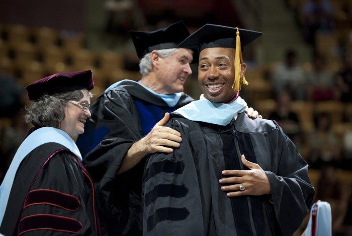A graduate stands on stage with two professors in regalia.