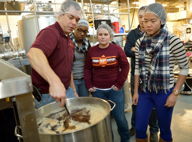 Faculty member works with students to stir a batch of beer